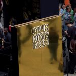 Gold mirror wall with Club Dirty Brew logo surrounded by guests