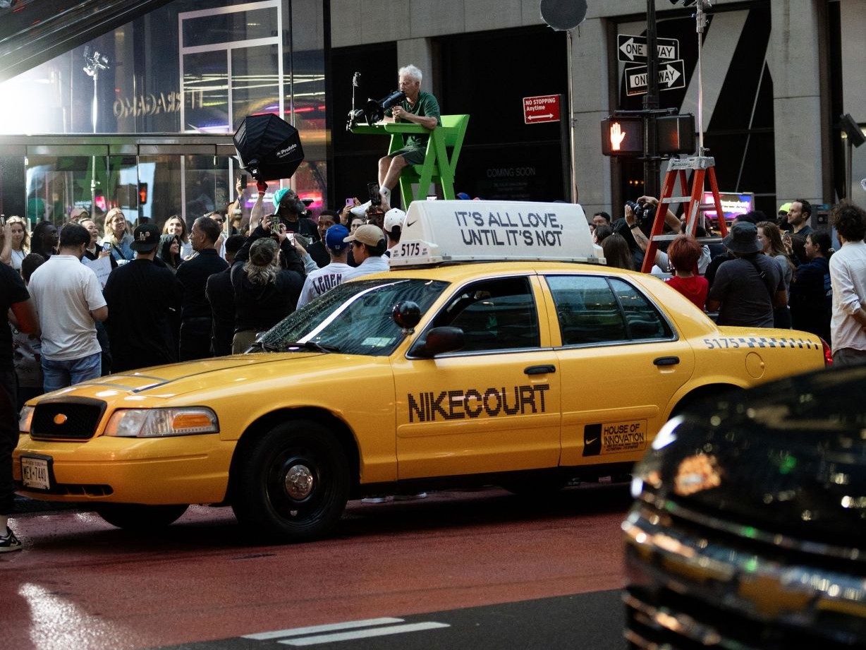 NikeCourt yellow cab street moment NikeCourt-branded Crown Victoria yellow cab with 'It's all love, until it's not' roof topper, crowd and umpire chair on a Manhattan street